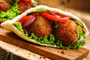 Falafel and fresh vegetables in pita bread on wooden table