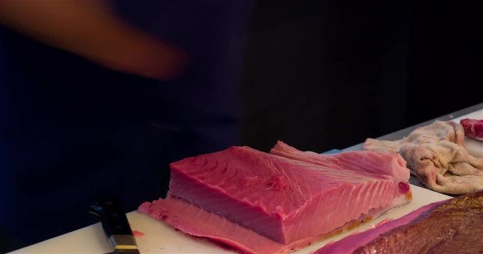 Chef hands cutting with knife raw bluefin tuna to filet pieces 4k video in sushi restaurant kitchen. Asian japanese cuisine.