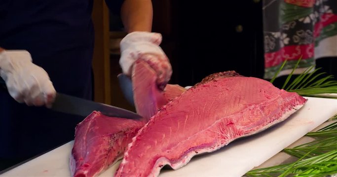 Chef hands cutting with knife raw bluefin tuna to filet pieces 4k video in sushi restaurant kitchen. Asian japanese cuisine.