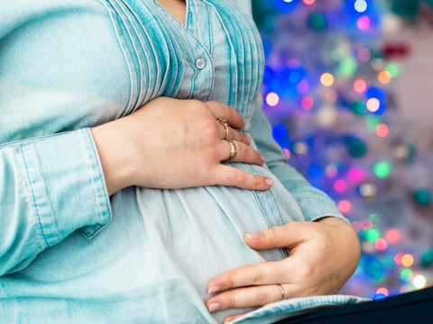Image of pregnant woman touching her belly with hands the background Christmas lights