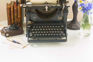black vintage typewriter with books on white wooden table with copy space