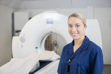 Young Professional Smiling By MRI Machine In Clinic