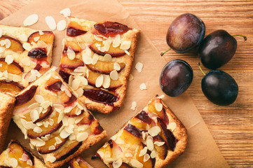 Slices of plum pie on brown wooden background.