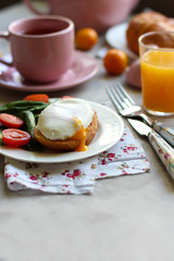 Breakfast with the poached egg on toast with spinach, tomatoes and orange juice, cup of tea coffee on kitchen the table