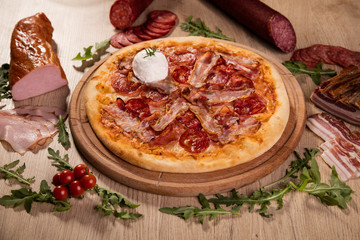 Pizza served on wooden board and raw ingredients on table