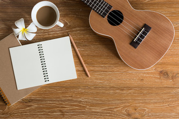 Ukulele on wooden background with note book and coffee 