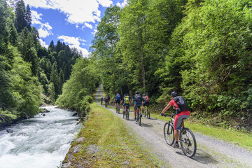 eine Gruppe Mountainbiker fährt entlang eines Wildbaches bergauf