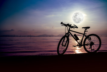 Fototapeta na wymiar Silhouette of bicycle on the beach against beautiful full moon 
