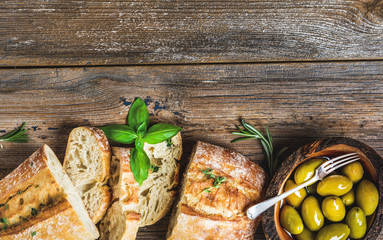 Green mediterranean olives in bowl and slices of freshly baked ciabatta over rustic wooden...