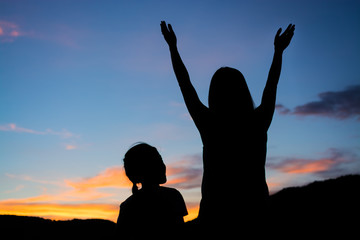 Silhouette of a woman open arms at sunset and girl look at her