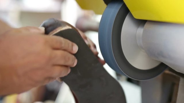 Calzolaio al Lavoro nella sua bottega artigianale. Levigatura suola di una scarpa. 