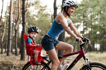 Plakat .Family biking in the forest. .Young beautiful mother with small son wearing helmets on bicycle.