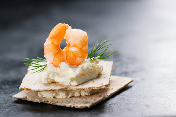 Appetizer canape with shrimp, cheese and dill on a small loaf of bread, closeup with copy space.