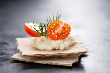Appetizer canape with cherry tomato, cheese and dill on a small loaf of bread, closeup
