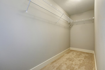 Empty narrow walk-in closet with shelves and carpet floor.