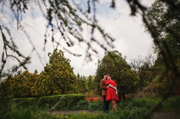 Couple hugging in love at park garden. Stylish man at velvet jacket and girl in red dress in love together