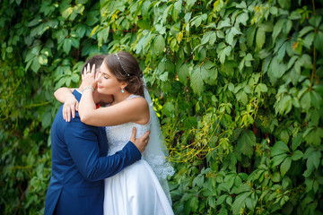 Beautiful happy young bride and groom, wall of green