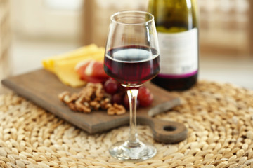 Glass with red wine and tasty snacks on a board on wicker mat