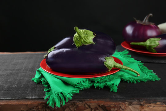 Fresh aubergines on red plate with green napkin on black background