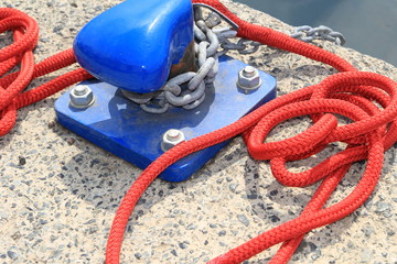 Closeup of blue harbour bollard with red rope on a concrete harbour quayside