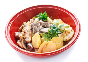 meat with mushrooms and vegetables in a pot on white