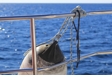 Fender ball or anchor ball hanging from the shiny chrome handrail of a boat with blue sea in background