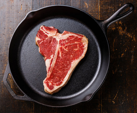 Raw fresh meat T-bone steak on cast iron frying pan on wooden ba