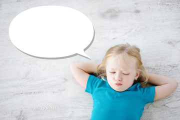 Fototapeta premium Little girl lying on white wooden floor with a speech bubble above her head