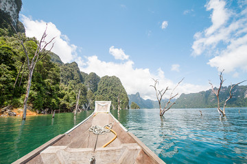 Head of wooden boat cruising in the lake with mountains view and cloudy blue sky background in Surat thani, Thailand
