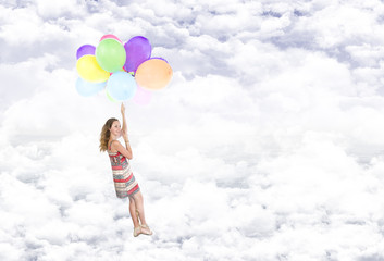 Girl hanging on balloons flying in the clouds