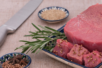 raw meat with spices and herbs in a square plate on a textured tissue