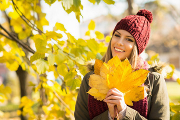 Happy young woman in autumn in park holding leaves