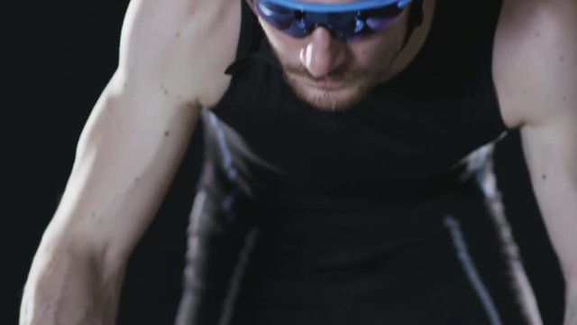 Sport cyclist in goggles and helmet and tight outfit 007. Healthy man wearing helmet and cycling glasses riding bicycle. Fitness workout  indoors on black background. Exercise in gym. Medium close up.