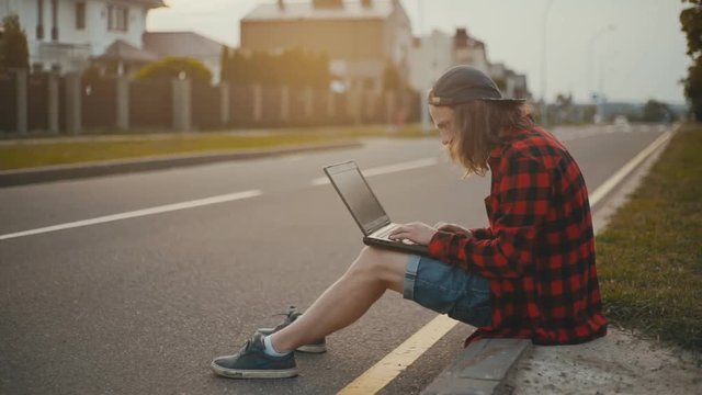Young man sitting on a city street and using a laptop