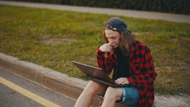 Young man sitting on a city street and using a laptop
