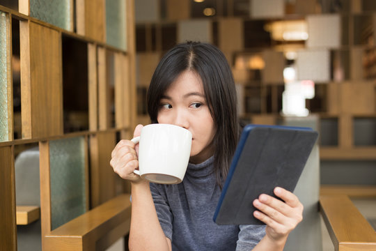 Woman drinking coffee / tea and using tablet in a coffee shop