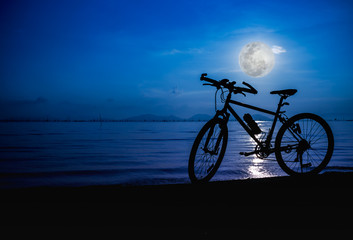Fototapeta na wymiar Silhouette of bicycle on the beach against bright full moon. Outdoors.