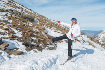 cute smiling girl fooling around in the snowy mountains balancing on one ski next to the ski slope in the sun in the winter