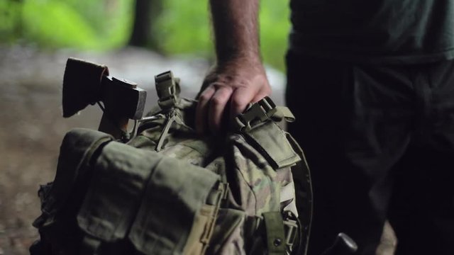 A camouflage backpack with an axe on it, and hiker’s hand resting on top.