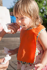 child eating ice cream from stick in woman hand