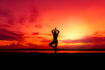 Silhouette healthy woman doing yoga exercises on the beach with sunset morning at Phuket, Thailand