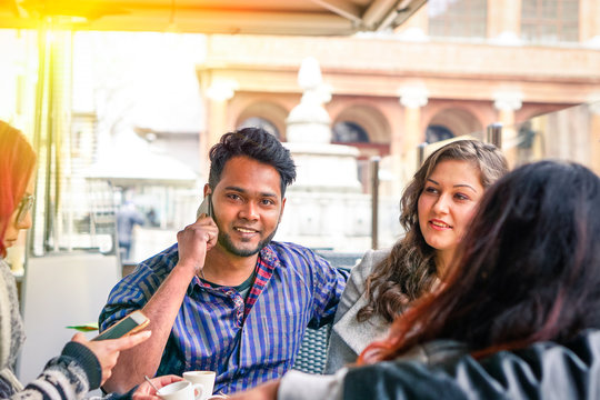 Multiracial friends using phone inside cafe bar restaurant at sunset 