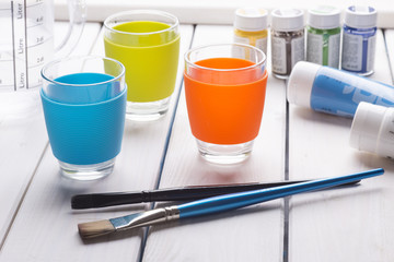 Still life of colorful cups, brushes and paint on a white wooden table. Drawing set.