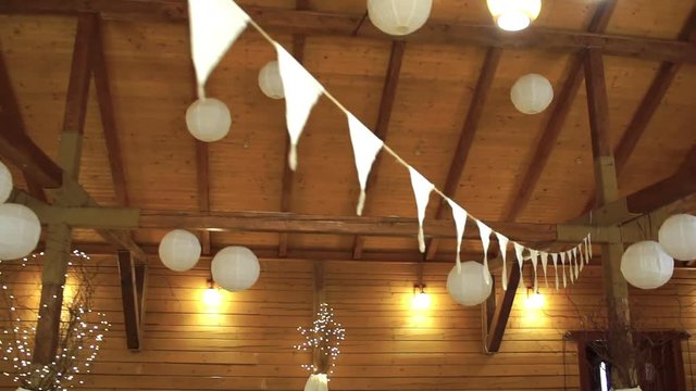 Wedding floristics in a rustic style. Festive hall with warm lights, burgee decor and china paper ball. Rural country wedding style using wildflowers and sunflower. Camera slide around