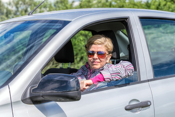 Happy blonde woman in sunglasses driving a new car