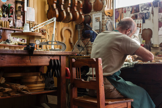 Violin maker in his workshop carving on neck of a new instrument