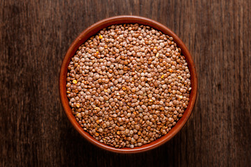 Rustic ceramic bowl of uncooked red lentils isolated on dark wood from above