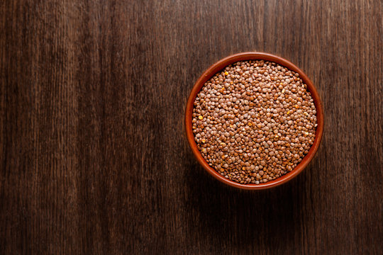 Rustic ceramic bowl of uncooked red lentils isolated on dark wood from above
