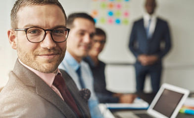 Cute man in eyeglasses with co-workers in meeting