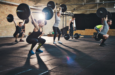 Adults lifting large barbells in fitness class - obrazy, fototapety, plakaty